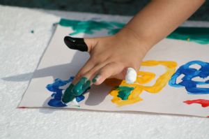 Child finger painting a yellow house and a blue cloud.